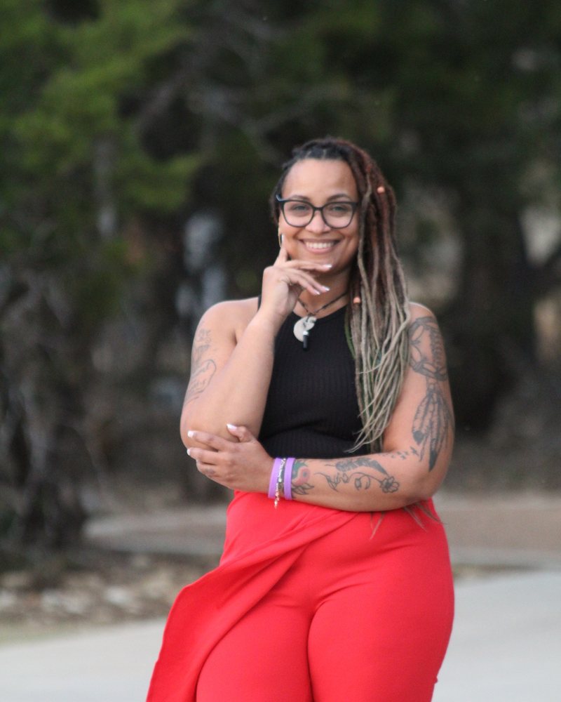 Ashia Walker smiling outdoors, in a black top and red trousers.