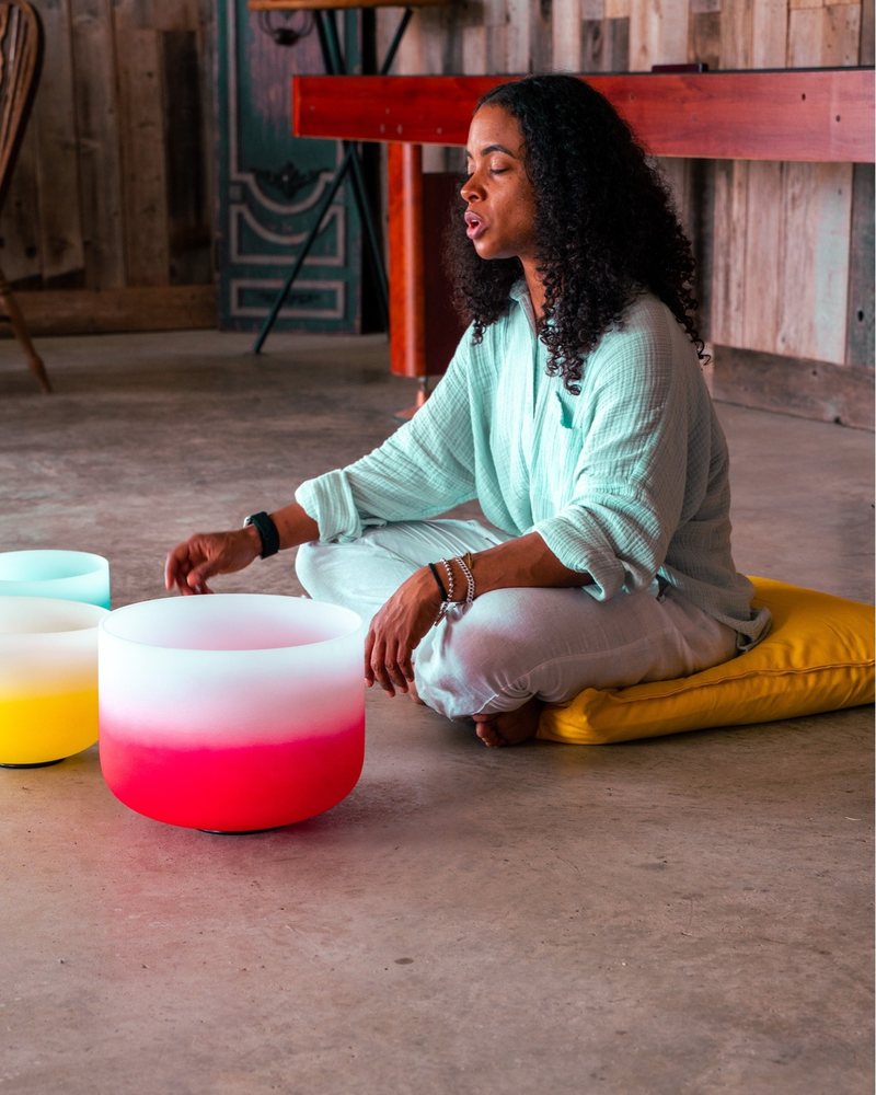 Shonda Colbert seated beside crystal singing bowls, eyes closed.