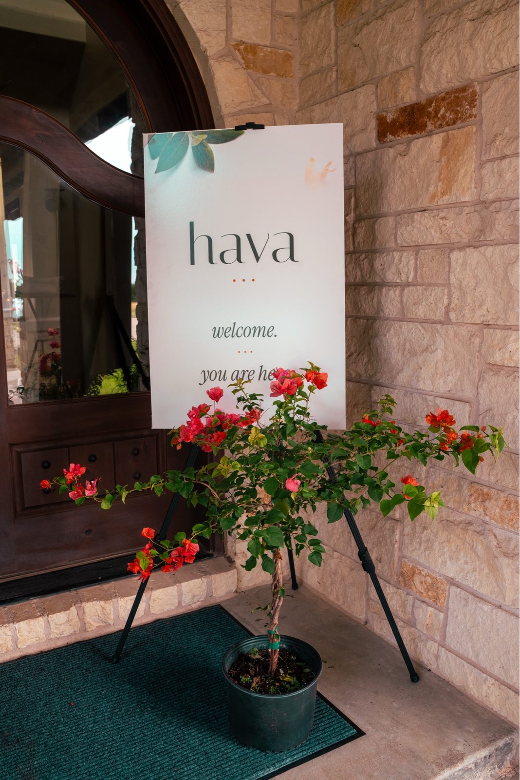A welcome sign at the door reads hava · welcome · you are here, beside a potted bougainvillea.